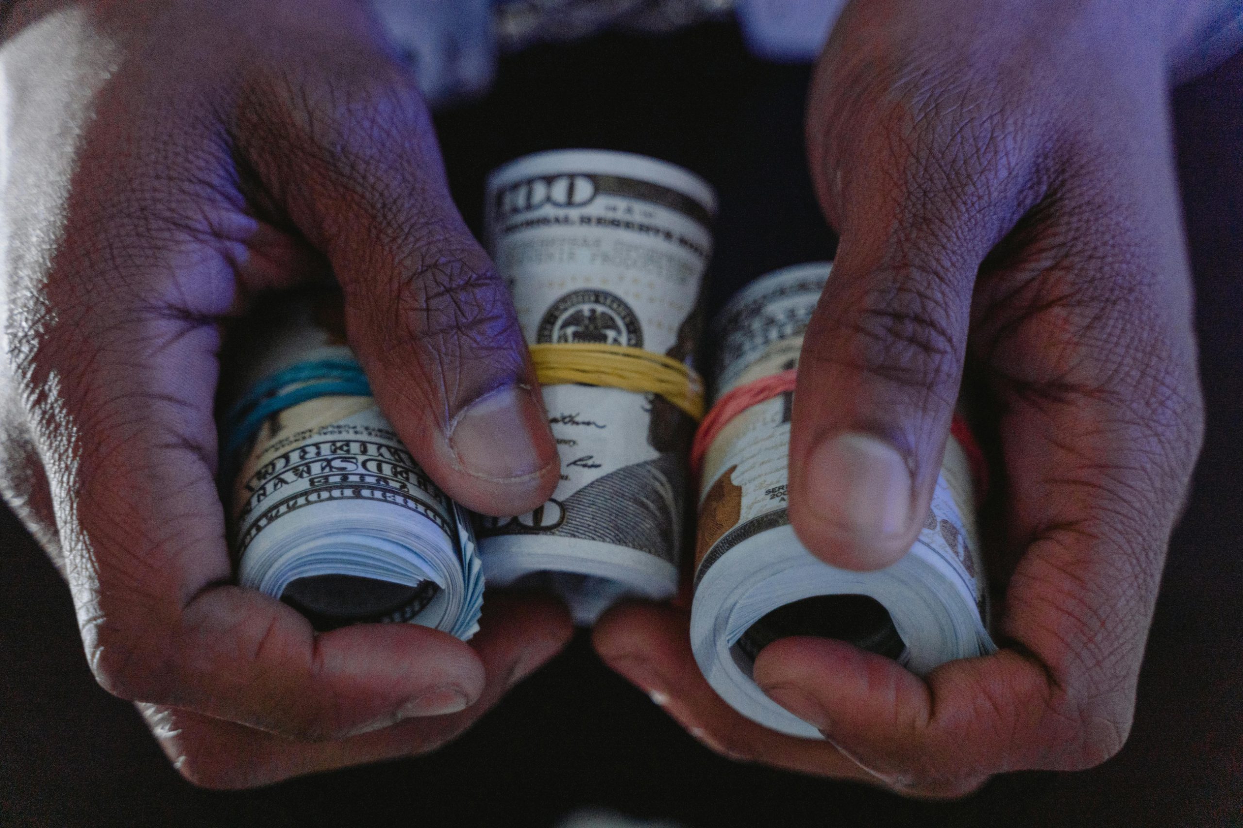 hands holding $100 bill rolls